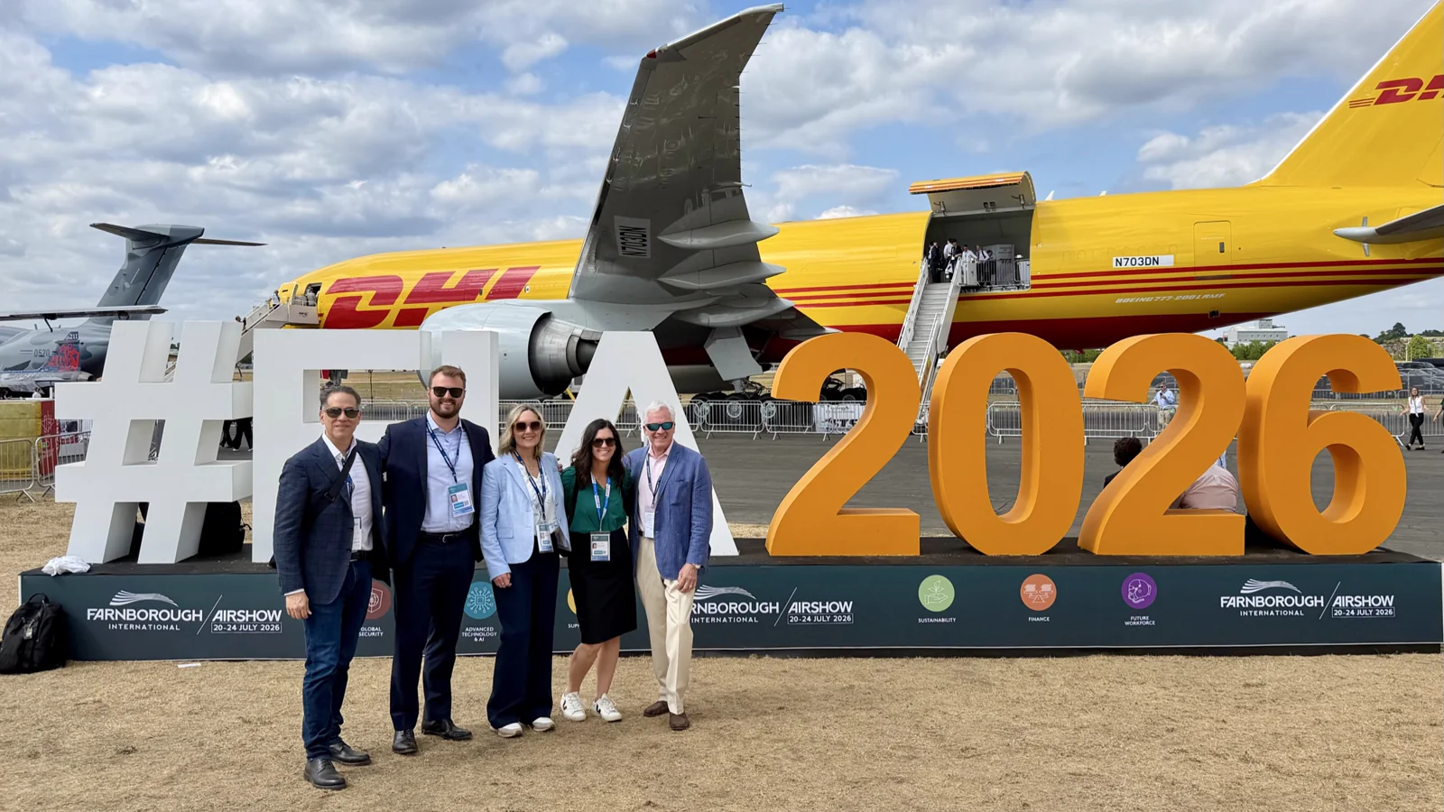 Jose J. Ruiz with IMD International Search Group Aerospace Practice partners in front of the #FIA2026 sign at the Farnborough International Airshow, DHL Boeing 777 freighter in the background — Day 2, 21 July 2026.